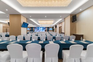 Un salón de conferencias con mesas dispuestas en filas, sillas blancas y una pantalla grande.
