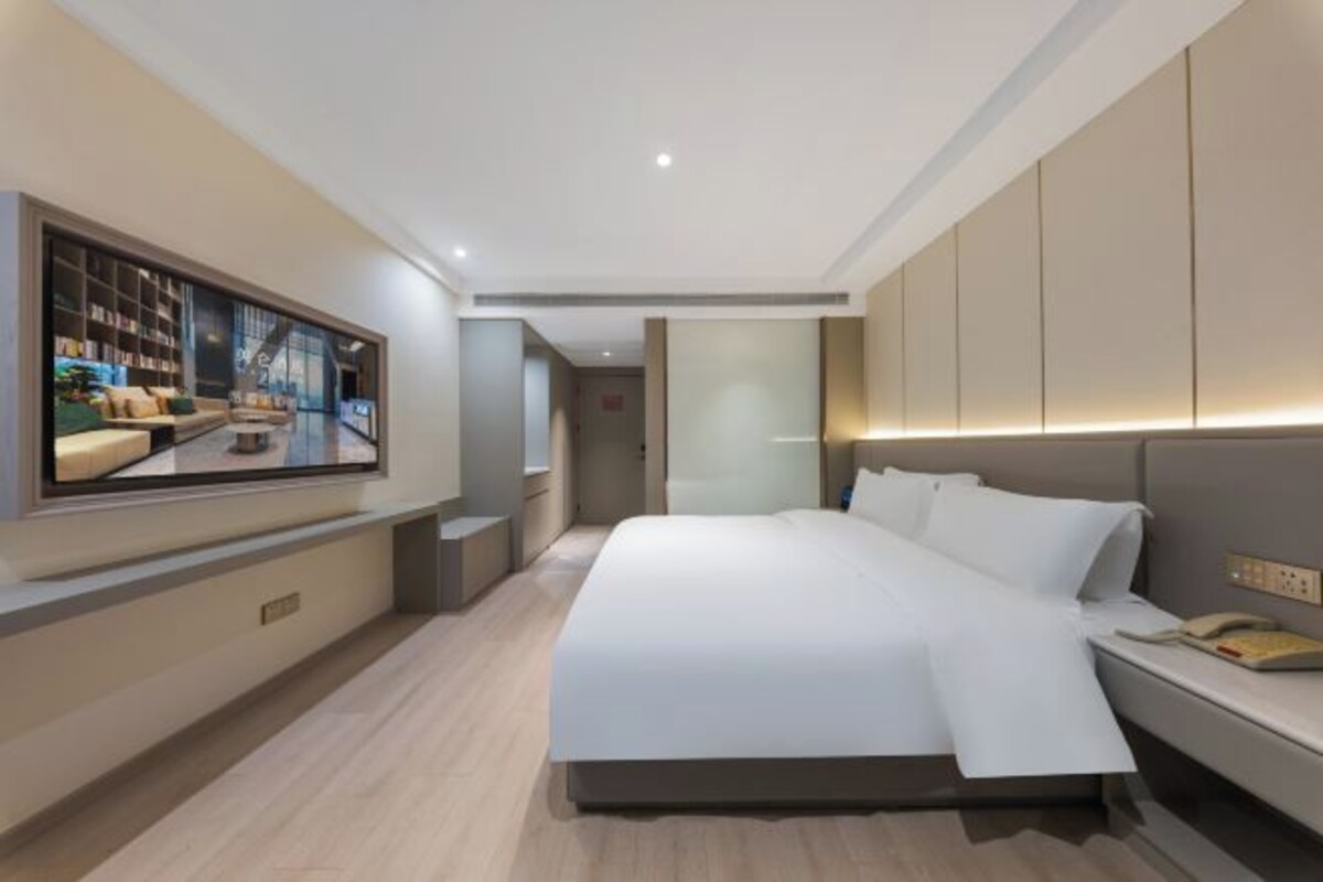Een moderne hotelkamer met een groot bed, een flatscreen televisie aan de muur en een nachtkastje met een lamp.