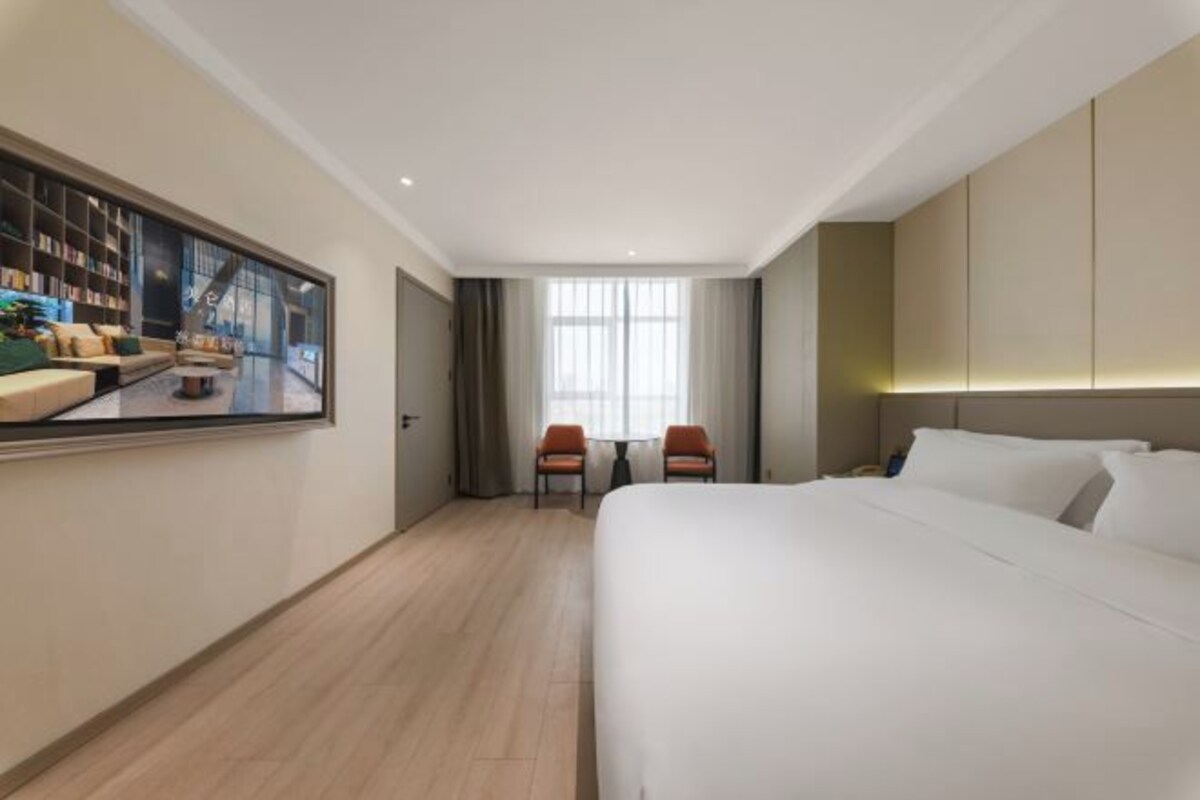 Een hotelkamer met een groot bed, een zithoek met stoelen, een televisie en een boekenkast.