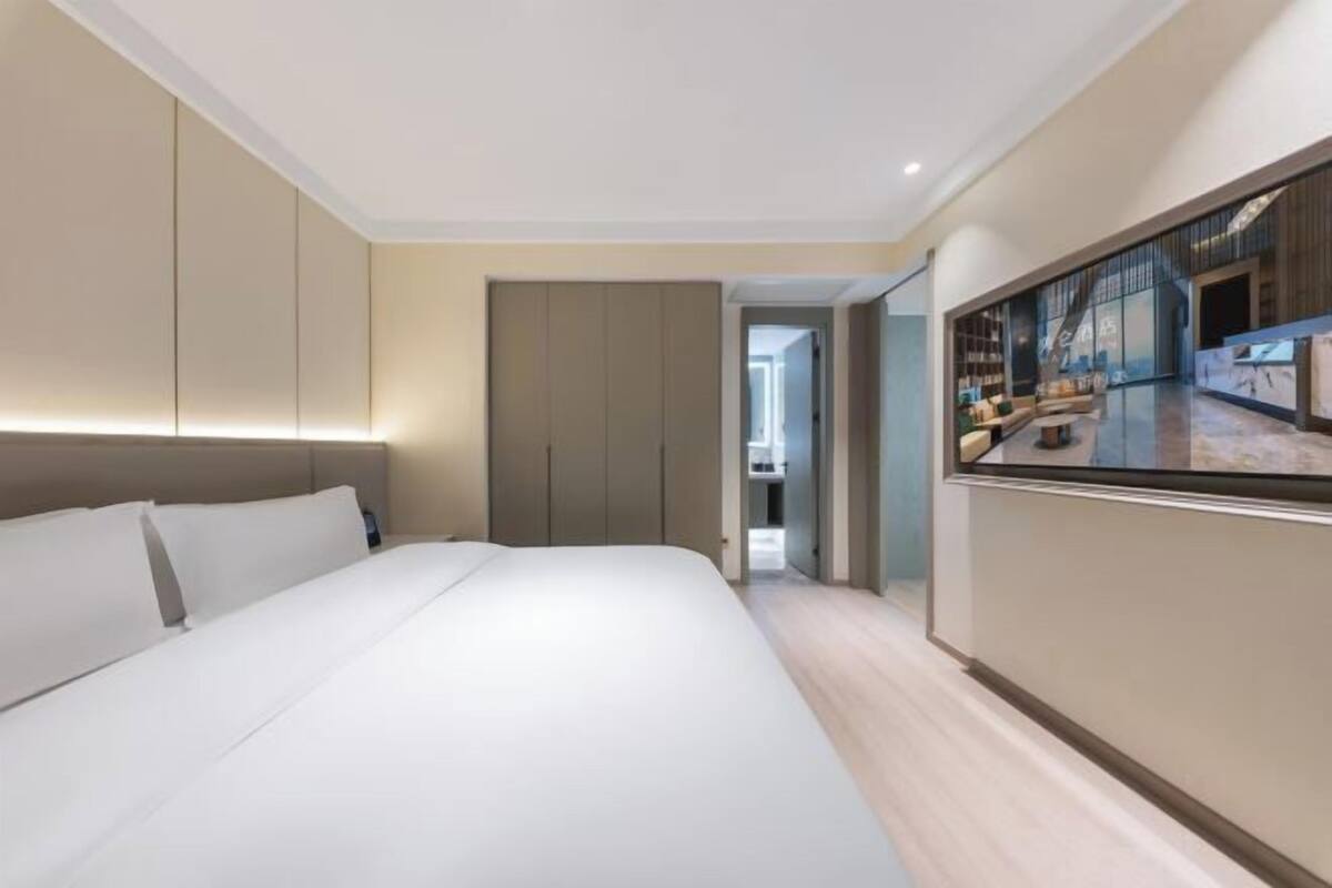 Ein modernes Hotelzimmer mit einem großen Bett, einem an der Wand befestigten Fernseher und Blick ins Hotelinnere.