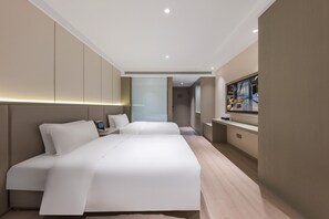Una habitación de hotel moderna con una cama grande, mesitas de noche, un televisor y vista al vestíbulo del hotel.