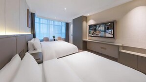Une chambre d’hôtel avec deux lits, un téléviseur fixé au mur et une grande fenêtre donnant sur la ville.