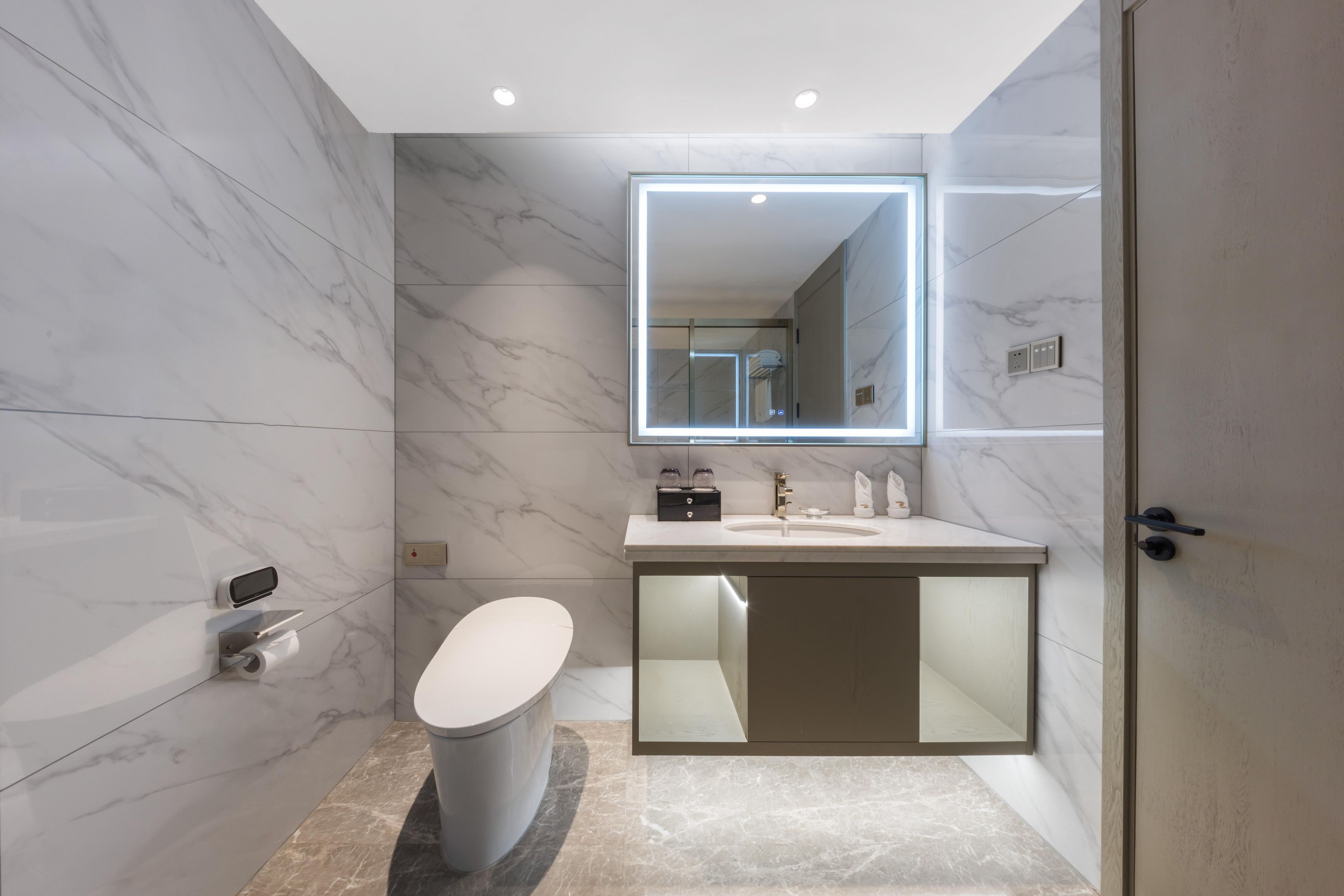 A modern bathroom with a marble floor, a toilet, a sink with a mirror, and a shower area.