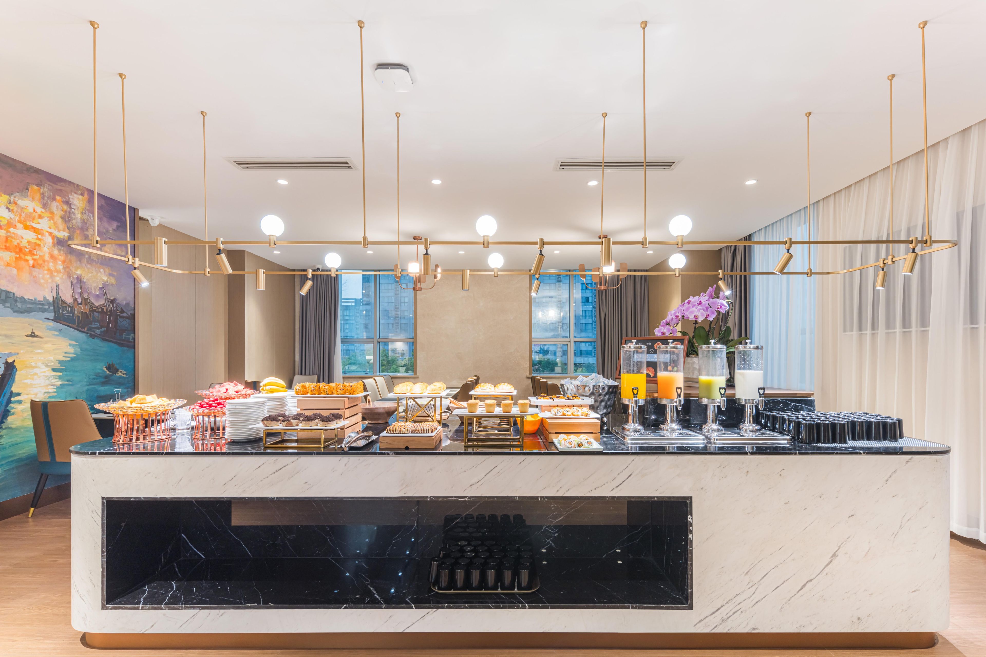 A hotel reception area with a marble counter, various food items, and a painting on the wall.