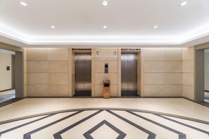 Een modern liftgedeelte met twee liften, een prullenbak en een vloer met een patroon.