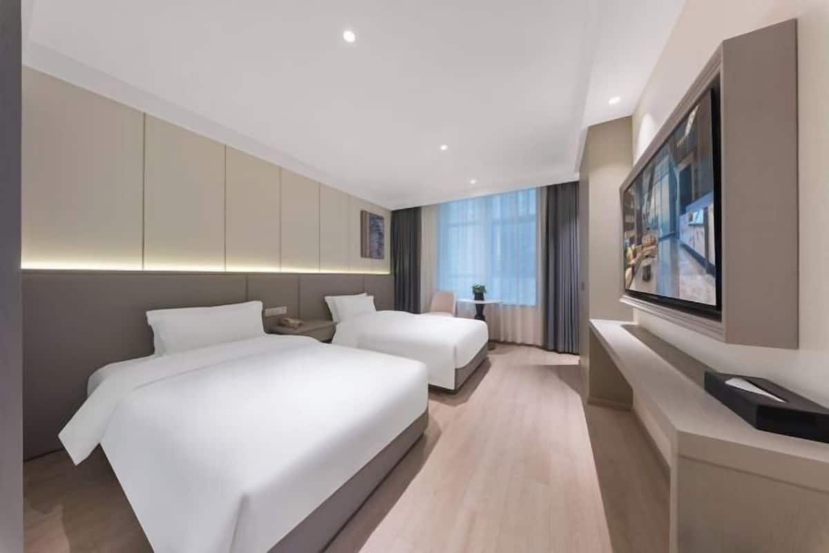Ein modernes Hotelzimmer mit zwei Betten, einem Flachbildfernseher und einem großen Fenster mit Vorhängen.