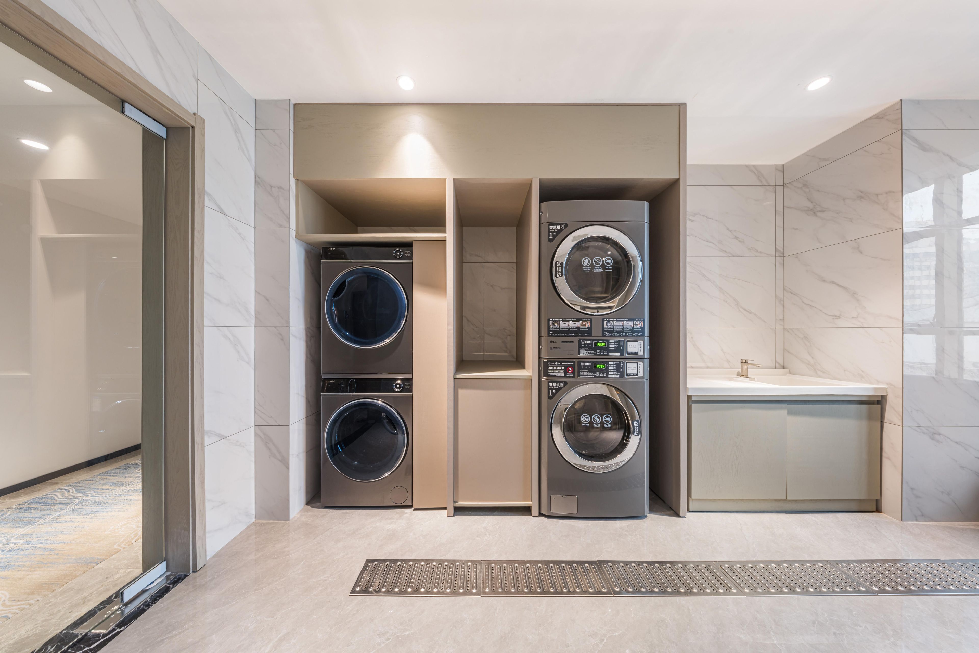 A modern laundry room with two front-loading washing machines, a built-in sink, and a marble-tiled floor.