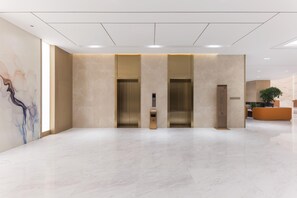 Un hall d’entrée moderne avec un sol en marbre, trois ascenseurs et un comptoir d’accueil.