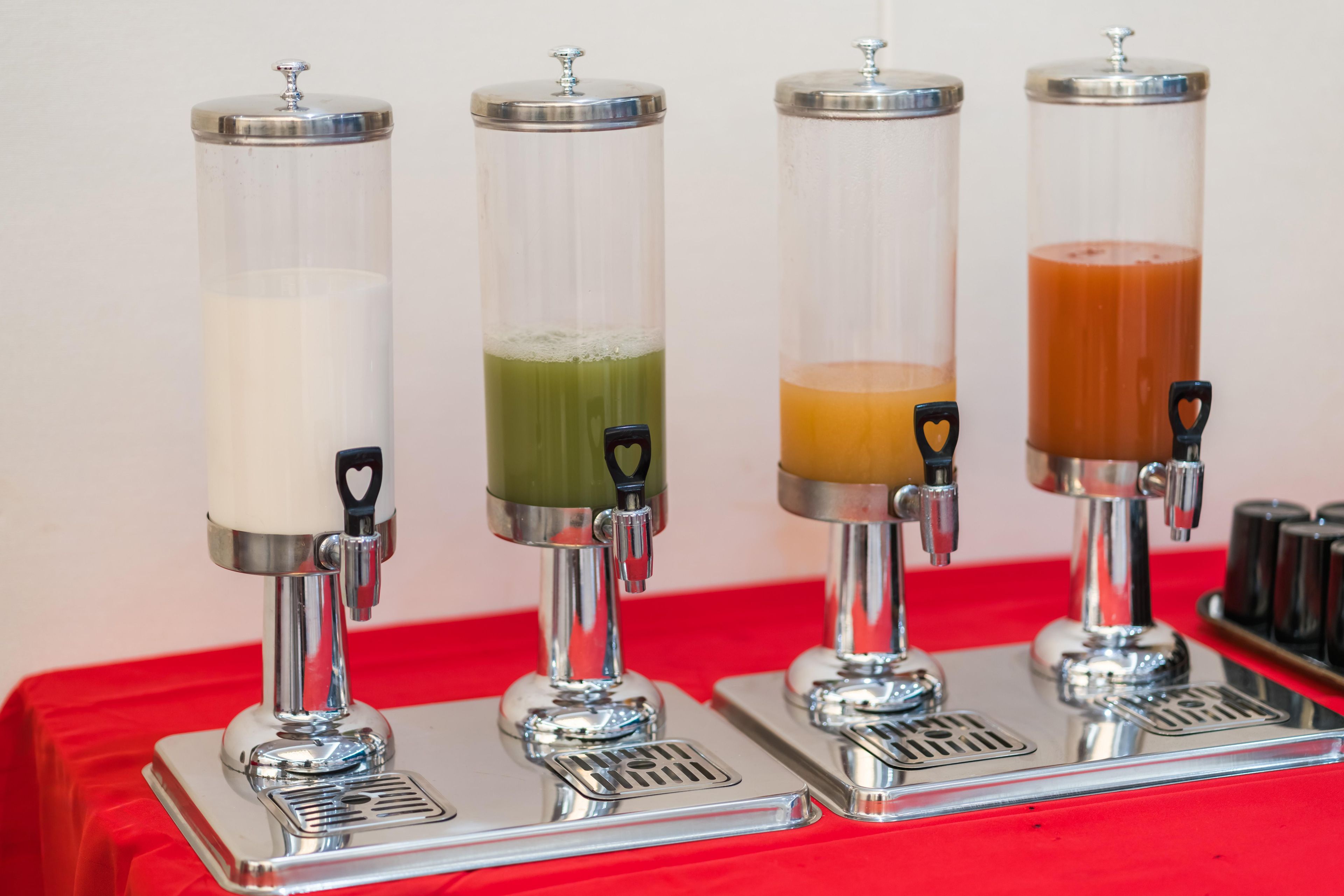 Vier drankdispensers met transparante bakken op een rode tafel.