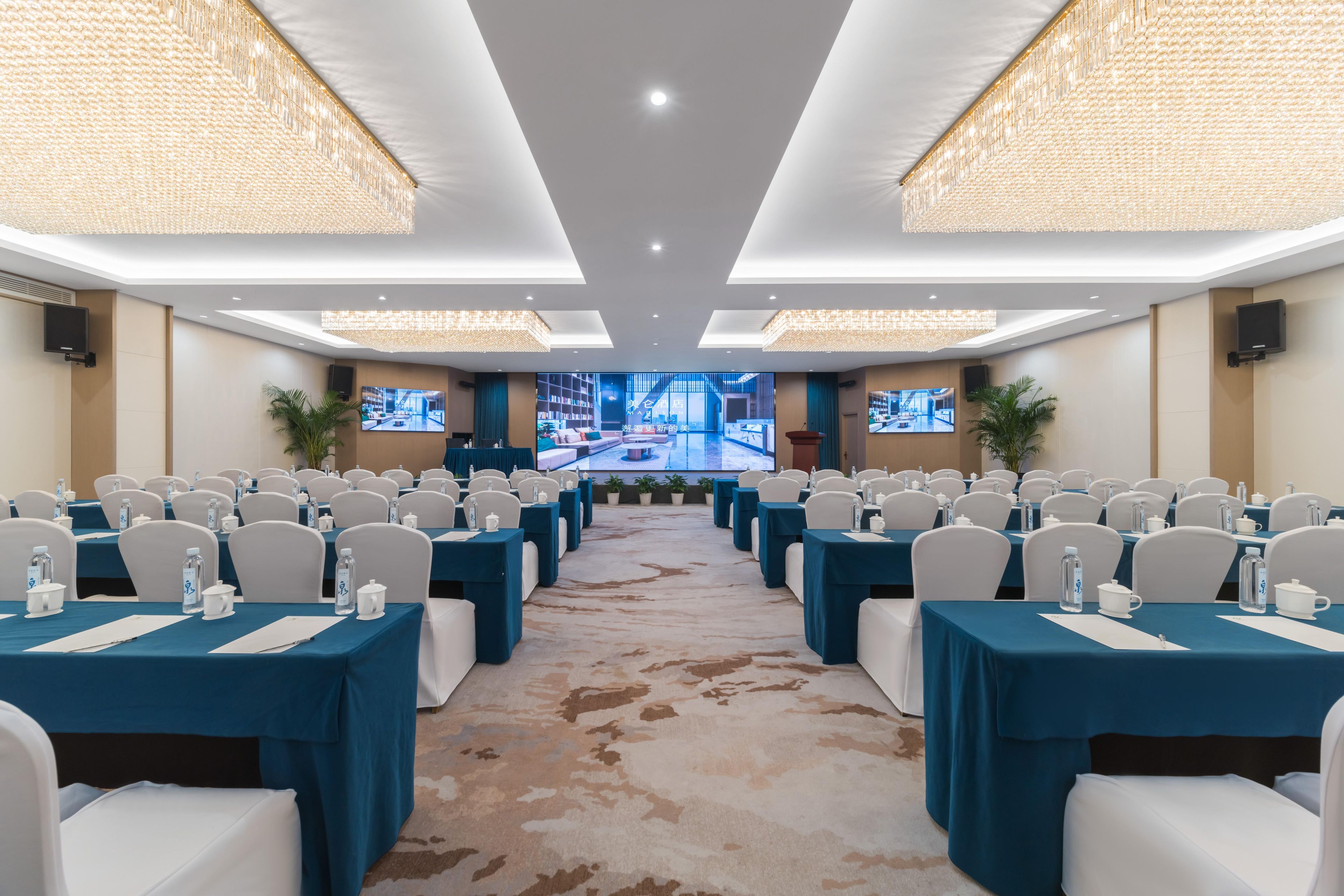 A conference room with rows of tables, chairs, and a large screen at the front.