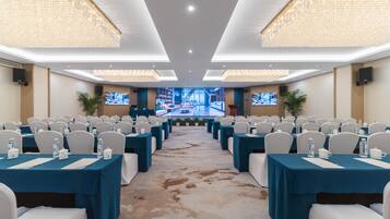 A conference room with rows of tables, chairs, and a large screen at the front.