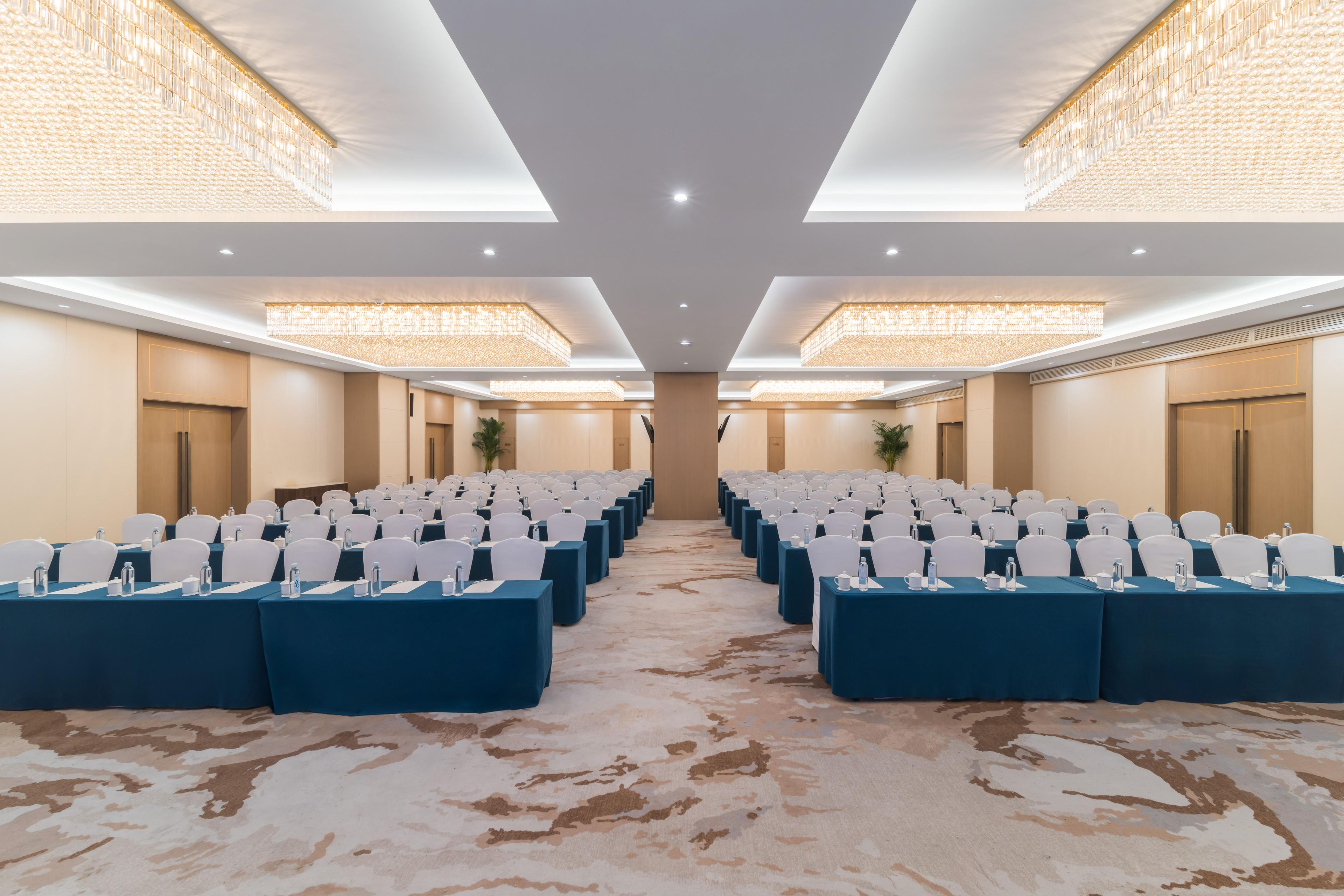 Una sala conferenze con file di tavoli e sedie, una moquette decorata e un lampadario.