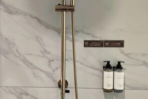 Une salle de bain avec un mur en marbre, une pomme de douche dorée et deux bouteilles de shampoing.
