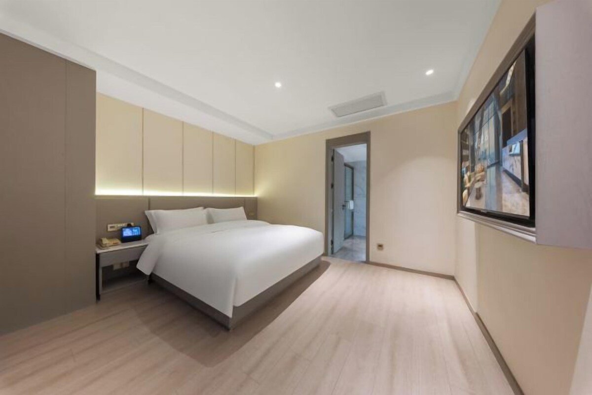 Une chambre d’hôtel moderne avec un grand lit, une table de chevet et une horloge numérique.