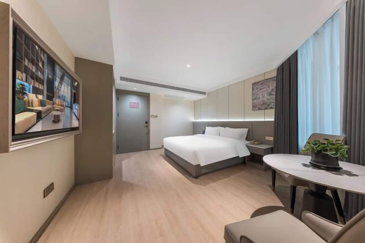 Ein modernes Hotelzimmer mit Bett, Nachttisch, Fernseher und einer kleinen Essecke.