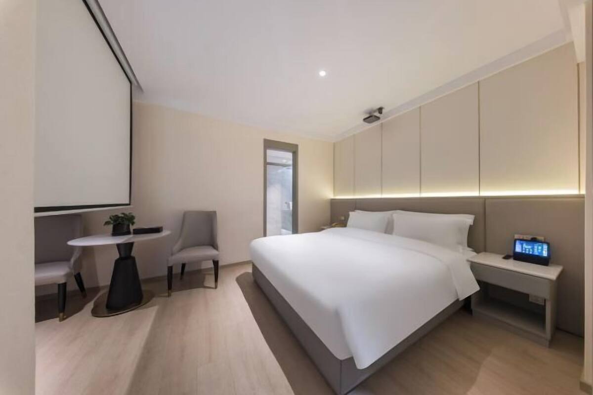Ein modernes Hotelzimmer mit einem großen Bett, Nachttischen, einer kleinen Sitzecke und einem großen Fenster.