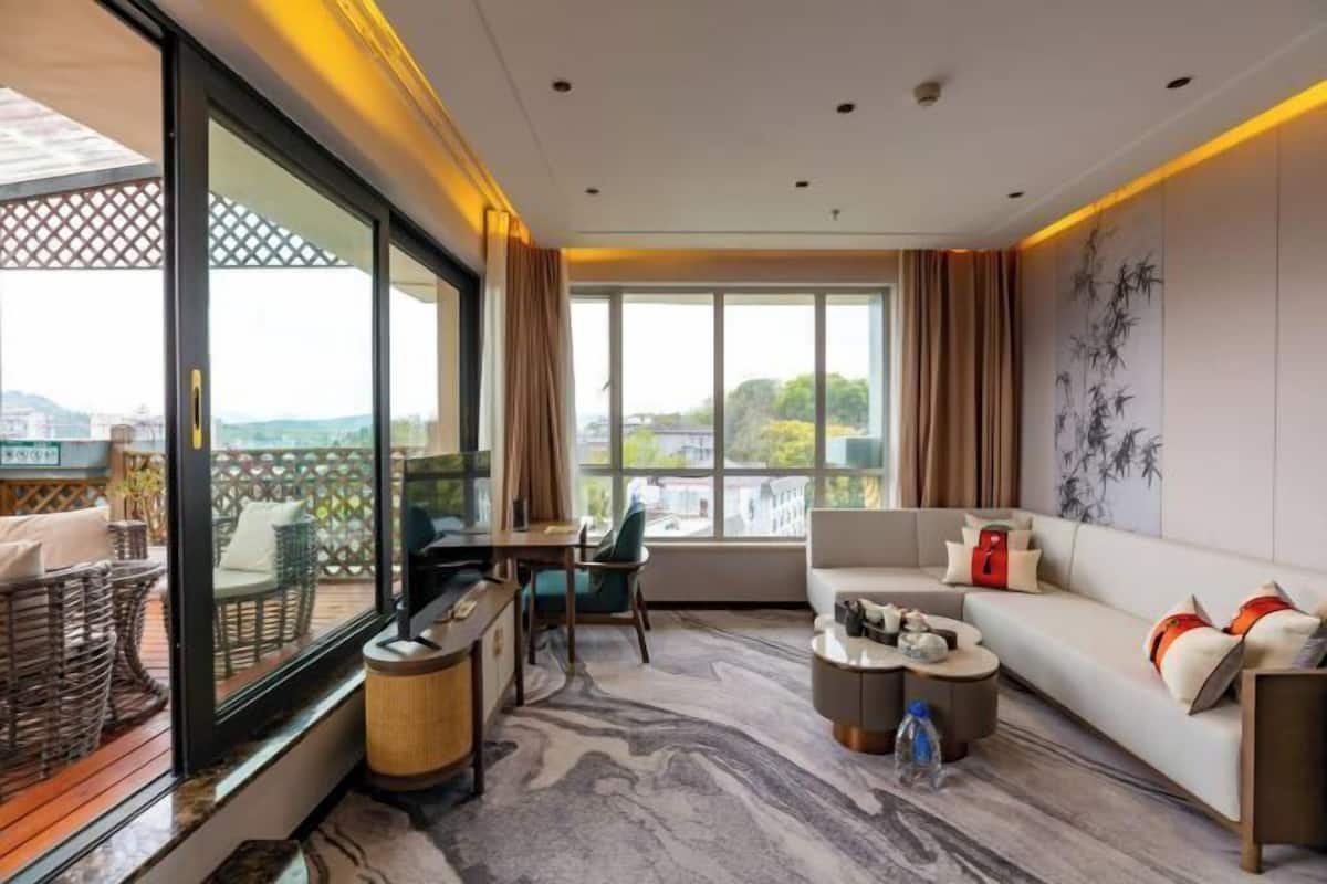 Habitación de hotel moderna con un ventanal grande, un sofá, zona de comedor y vistas a la ciudad.
