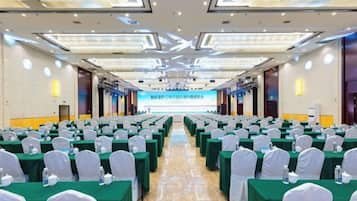 Un salón de conferencias con filas de mesas y sillas, una pantalla grande al frente y un escenario.