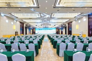 Un salón de conferencias con filas de mesas y sillas, una pantalla grande al frente y un escenario.