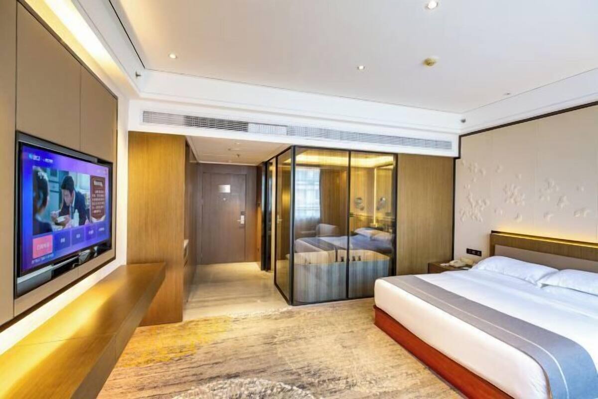 Una habitación de hotel moderna con televisión, cama, separador de vidrio y suelo de madera.