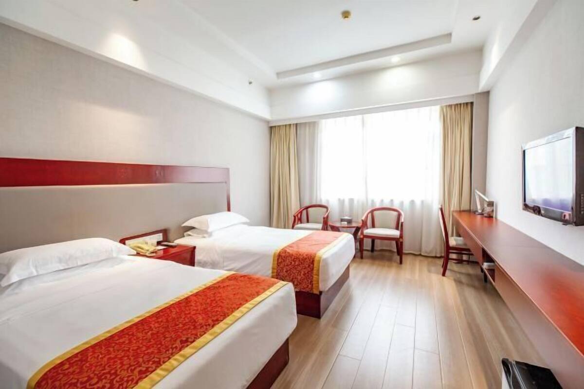 Habitación de hotel con dos camas, un escritorio, una silla, un televisor y una ventana con cortinas.