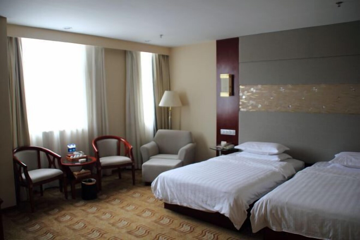 Une chambre d’hôtel avec deux lits, un bureau avec une lampe, une chaise et une vue sur l’extérieur grâce à de grandes fenêtres.