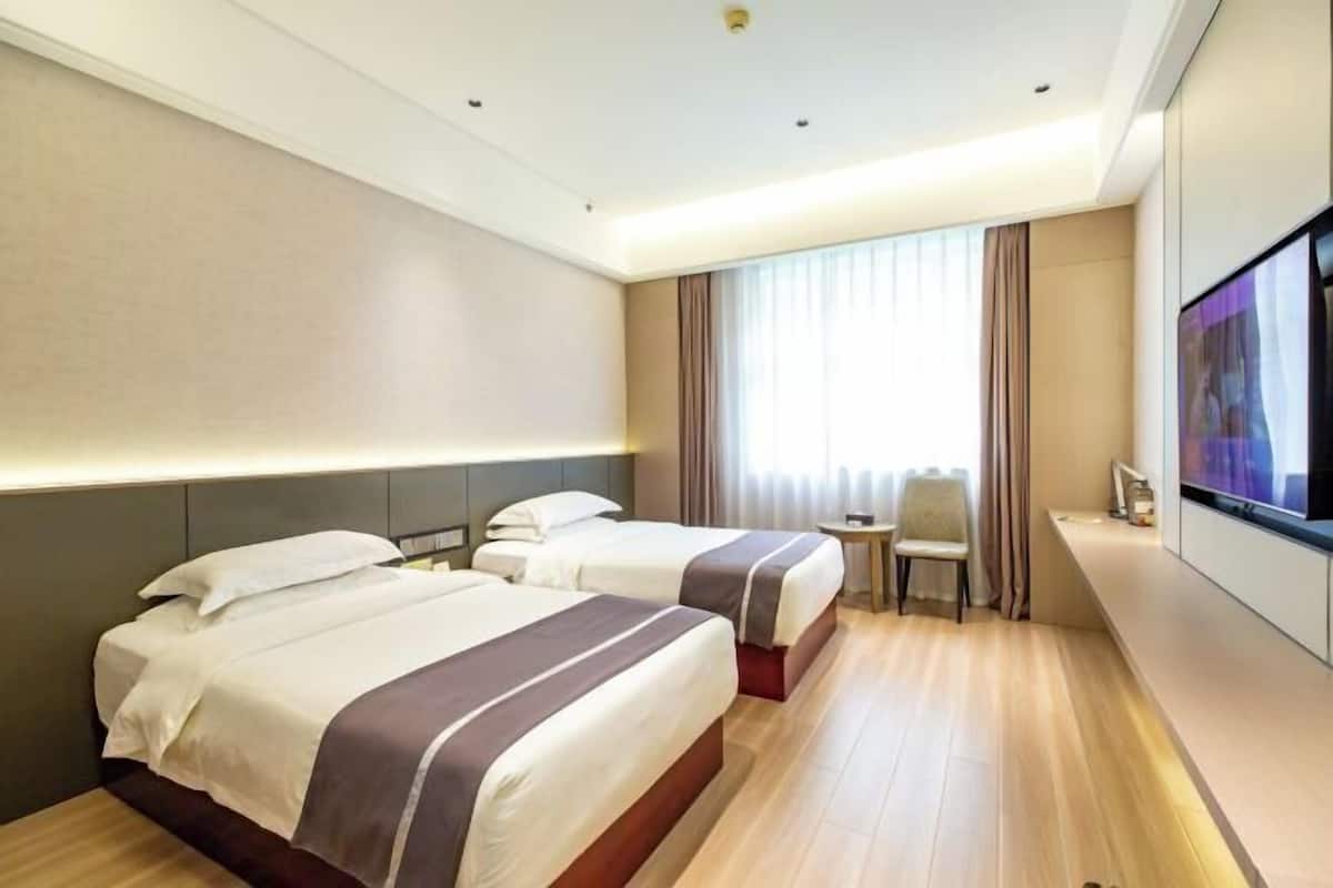 Una habitación de hotel con dos camas, televisión, una mesita y una ventana con cortinas.
