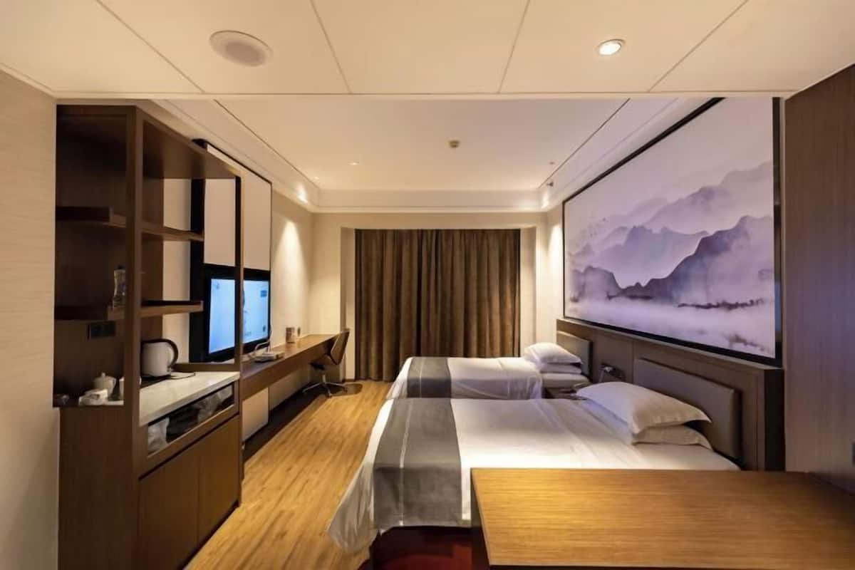 Una habitación de hotel con cama, escritorio, computadora, televisor y un cuadro grande en la pared.