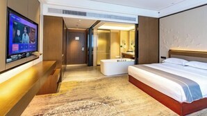 Une chambre d’hôtel moderne dotée d’un grand lit, d’un téléviseur à écran plat fixé au mur, d’une salle de bain séparée et d’un dressing.