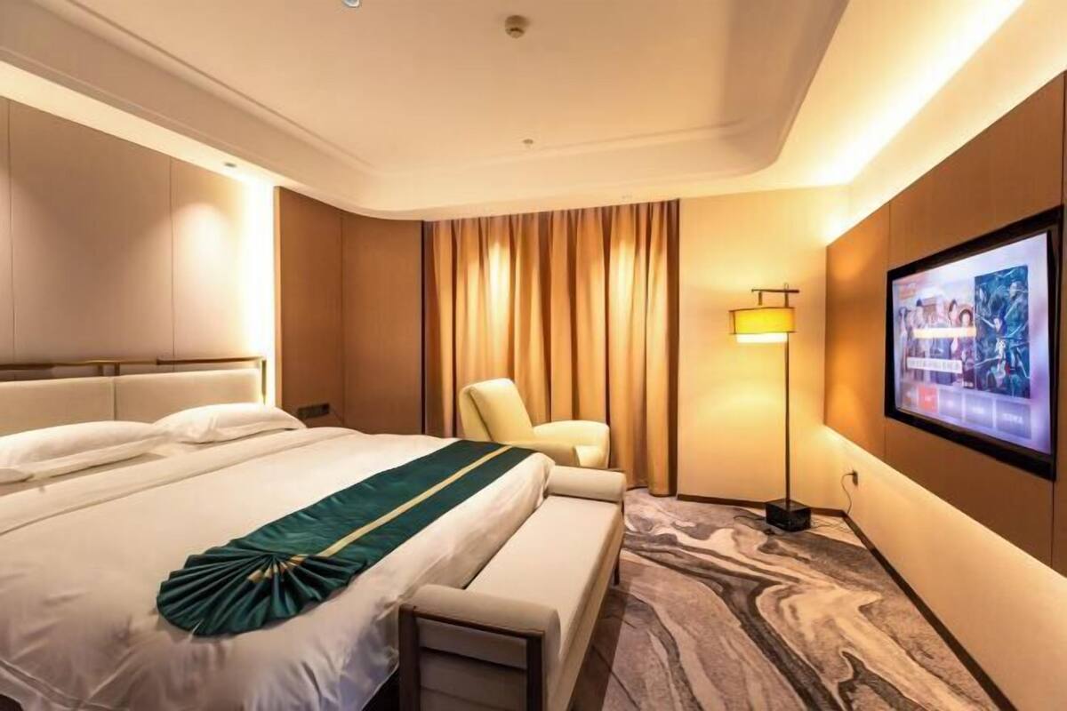 Habitación de hotel con una cama grande, zona de estar, televisión y pantalla montada en la pared.