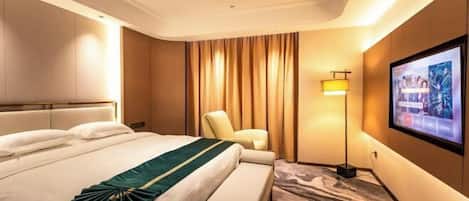 A hotel room with a large bed, a seating area, a television, and a wall-mounted screen.