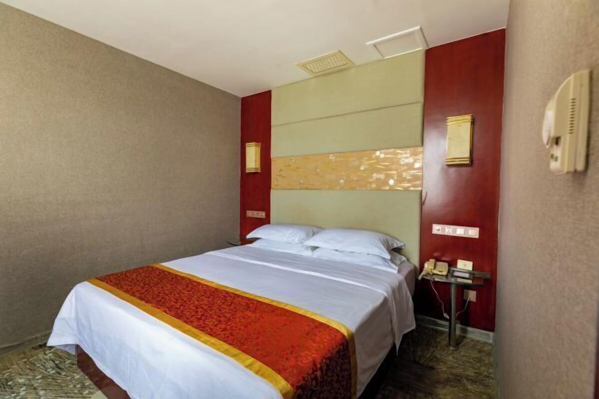 Une chambre d’hôtel équipée d’un lit, d’un téléphone et d’un luminaire fixé au mur.