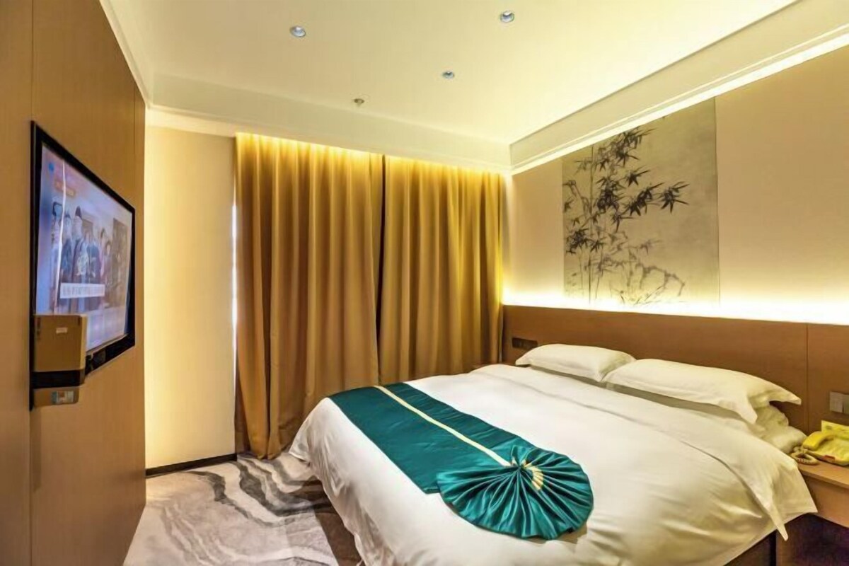 Une chambre d’hôtel avec un grand lit, un téléviseur à écran plat fixé au mur, un tableau au mur et un rideau à la fenêtre.