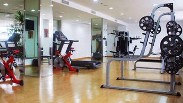 Un gimnasio con equipo de ejercicio, cinta de correr y pared de espejos.