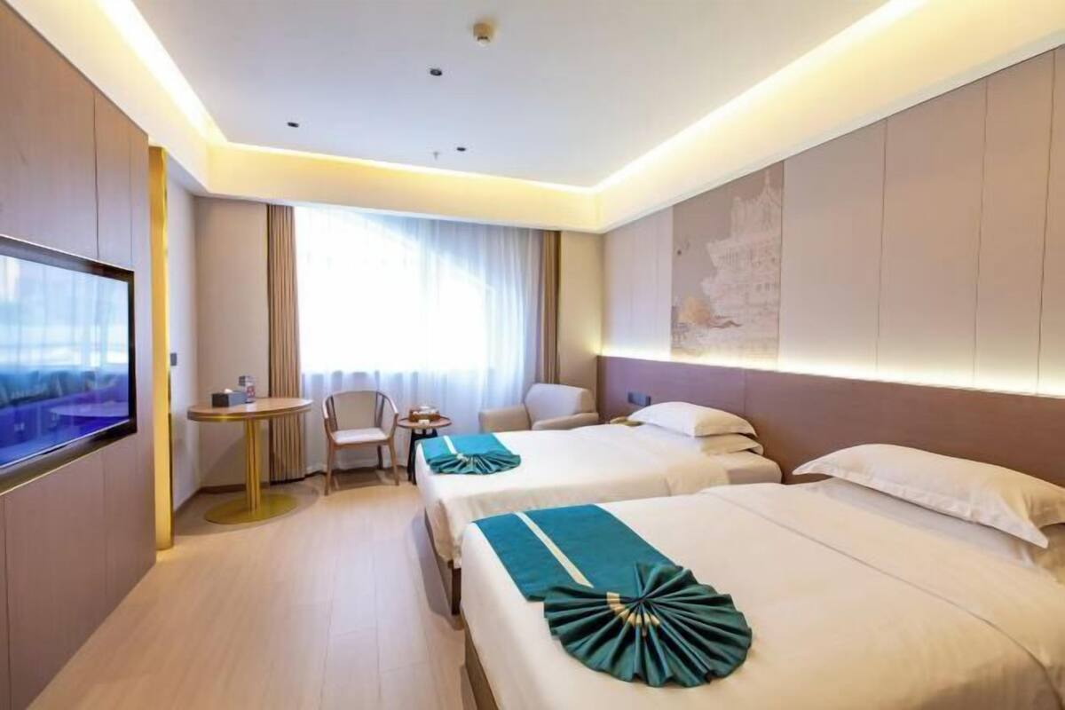 Habitación de hotel con dos camas, televisor, una mesita y ventana con cortinas.