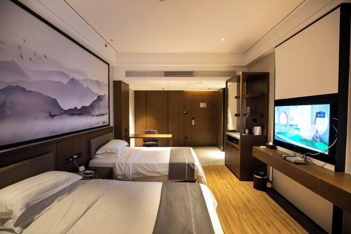 Una habitación de hotel con dos camas, televisión, escritorio y un cuadro grande en la pared.
