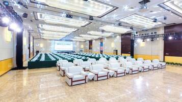 A conference room with rows of white chairs, a large screen at the front, and a stage with a podium.
