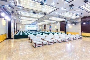 Une salle de conférence avec des rangées de chaises blanches, un grand écran à l’avant et une scène avec un pupitre.