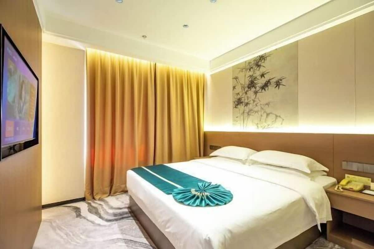 Habitación de hotel con cama, cortinas, una obra de arte en la pared y una mesita de noche con teléfono.