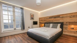 A modern bedroom with a large bed, wooden headboard, and a large window with curtains.