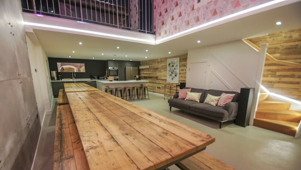 A modern kitchen with a central island, a dining area with a long wooden table, and a cozy seating area with a sofa.