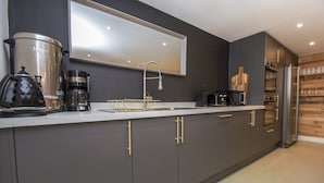 A modern kitchen with a stainless steel coffee maker, a sink, and a large mirror above the countertop.
