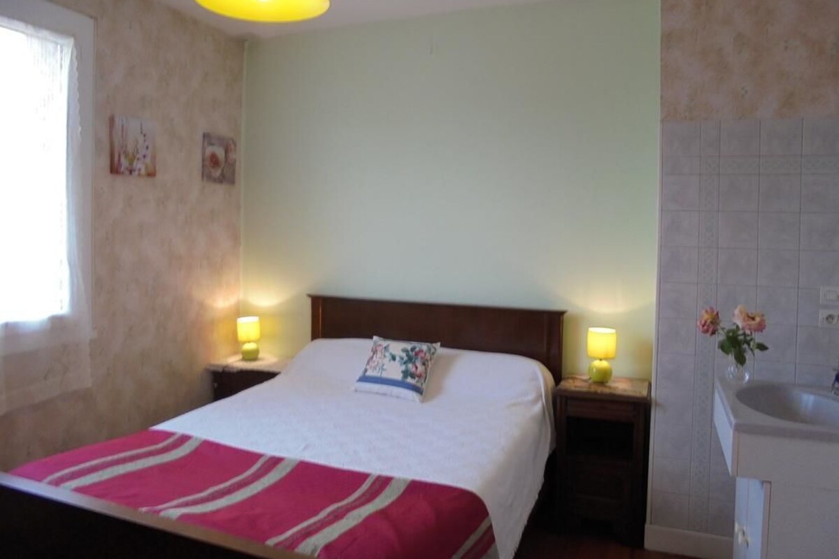 Ein Hotelzimmer mit einem Bett, Nachttischlampen, einem Fenster und einem Badezimmer mit Waschbecken.