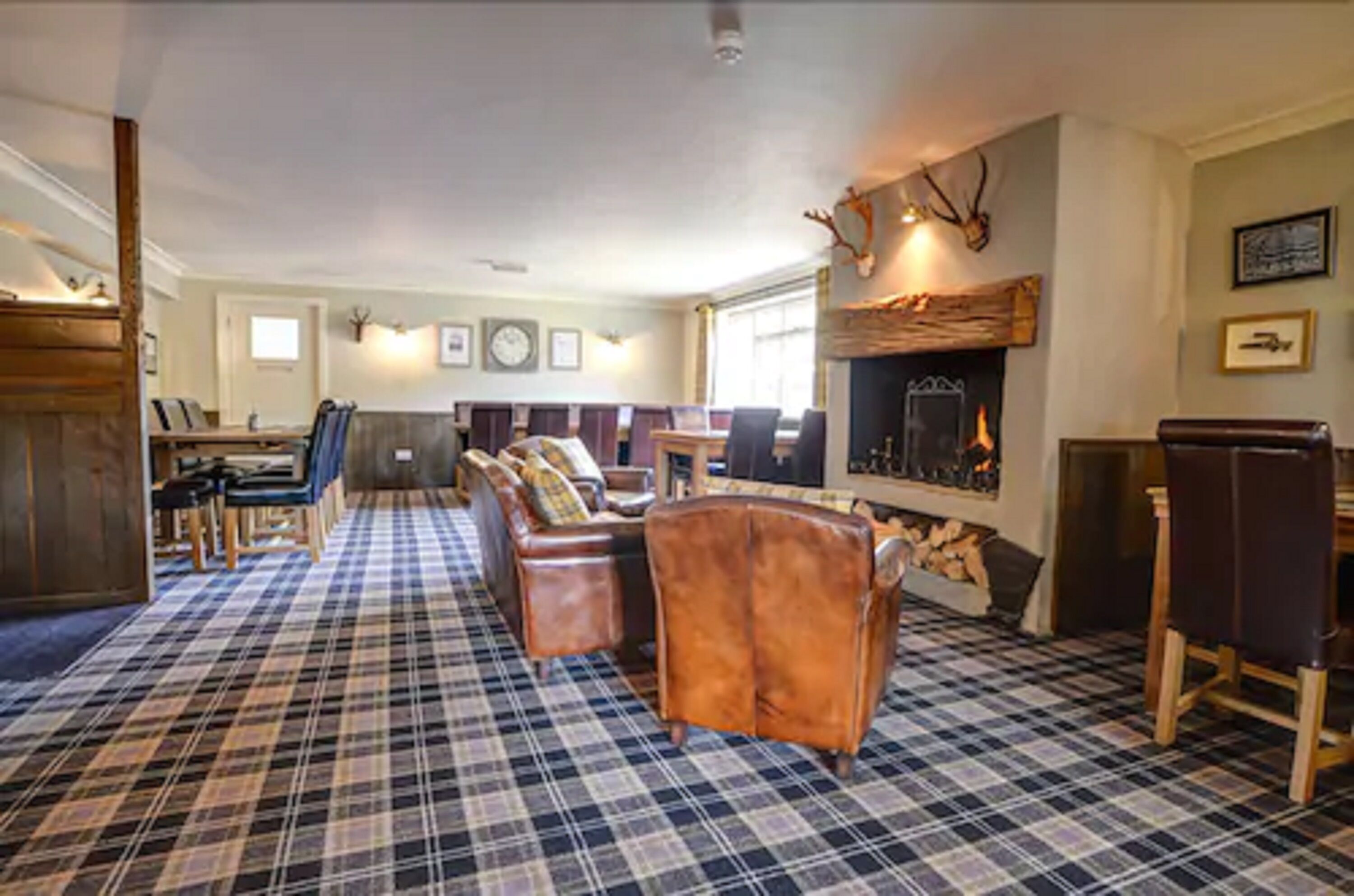 A spacious living room with a plaid carpet, leather sofas, a fireplace, and antler decorations.
