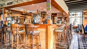 A bar area with wooden stools and a counter, surrounded by shelves with various items.