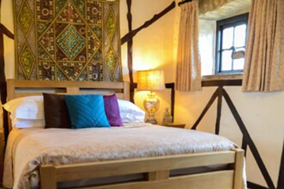 A bedroom with a wooden bed, a patterned tapestry, and a window with curtains.