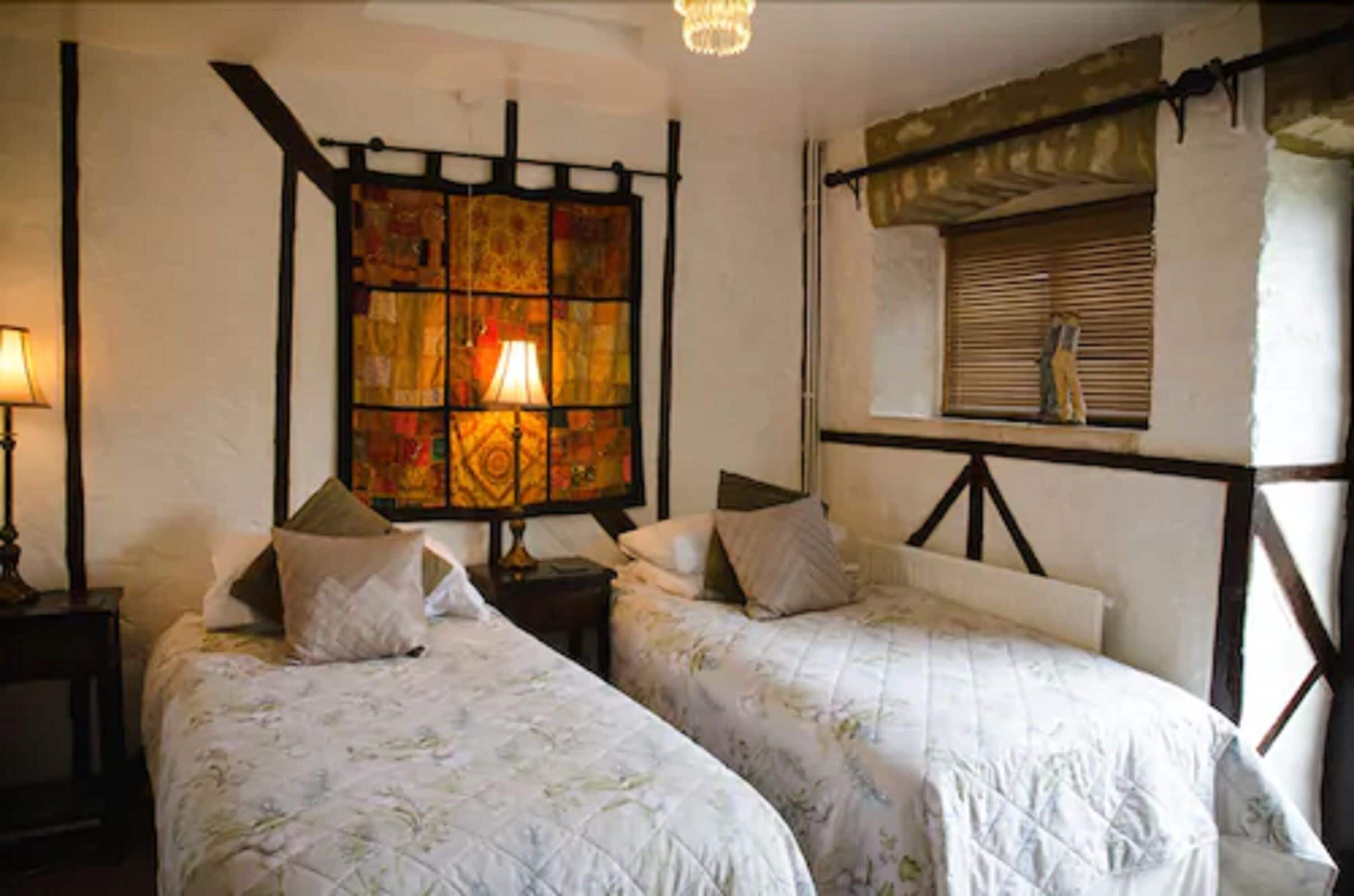 Una habitación con dos camas, un vitral y un ventanal con contraventanas.