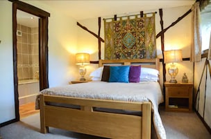Quarto com cama de madeira, duas mesas de cabeceira com abajures, uma cabeceira decorativa e um espelho.