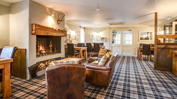 A cozy living room with a fireplace, plaid carpet, leather sofas, and a dining area with wooden furniture.