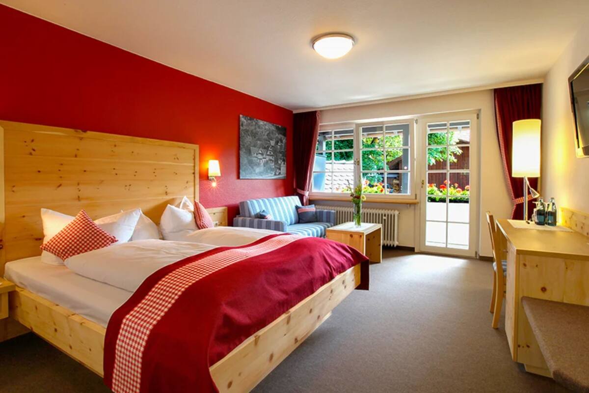 Ein Zimmer mit einem hölzernen Bett, einem Schreibtisch und einem Fenster mit Blick auf Grünflächen.